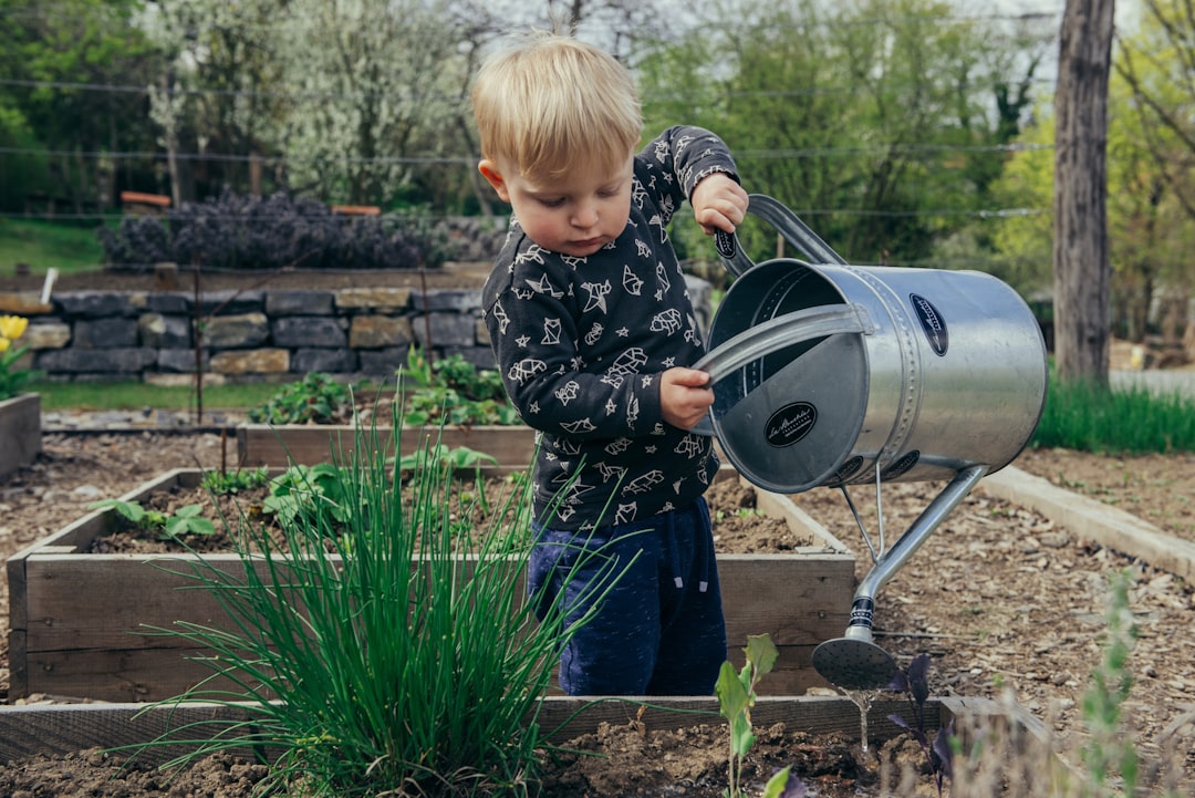 boy-in-black-and-white-long-sleeve-shirt-standing-beside-gray-metal-watering-can-during-daytime-ffj8qa0vqu0