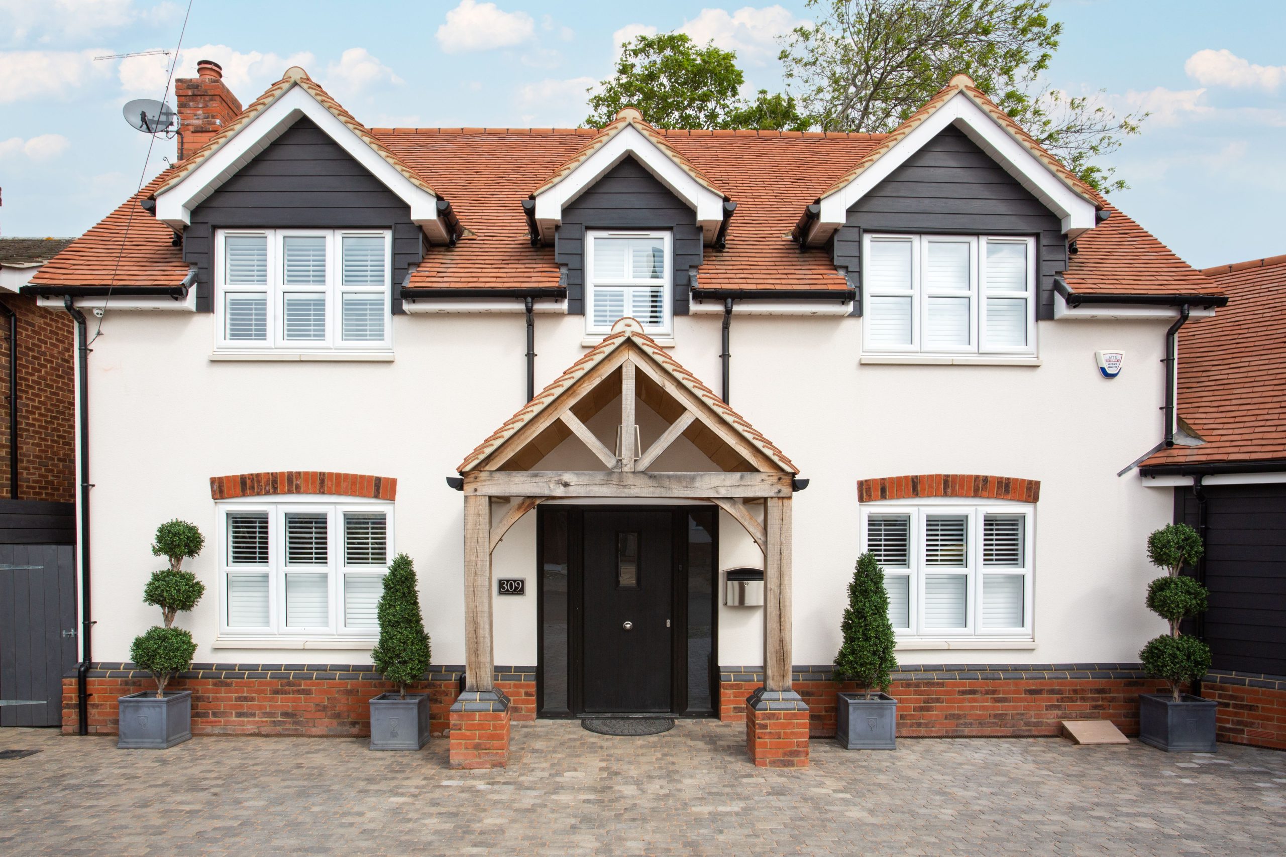 Two-story modern house in Colchester with traditional architecture, striking red tile roof, and manicured shrubs.