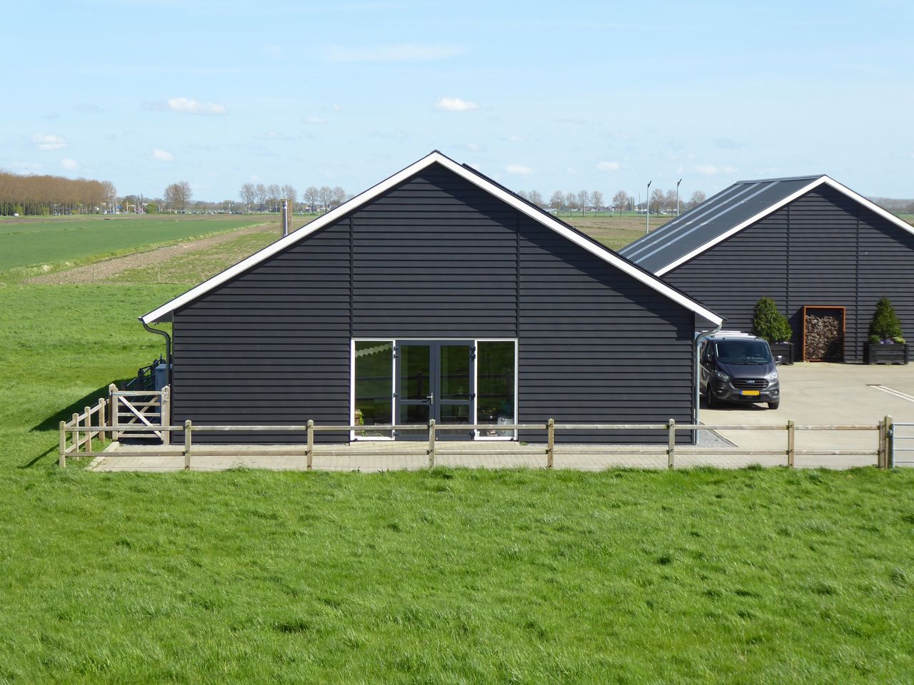 A contemporary black barn stands in a lush green countryside landscape under a clear sky.